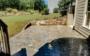 A stone wall and patio with trees in the background.